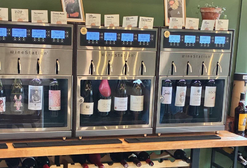 Three WineStation self-serve machines at Uncorked Wine Tastings, each with tasting note cards and pour options displayed above the dispenser